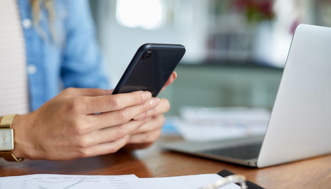 Kontaktieren Sie uns – Frau mit Smartphone und Notebook am Schreibtisch